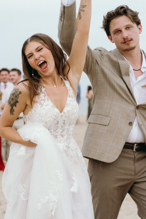 A joyful bride in a white lace dress and groom in tan suit celebrating during their wedding ceremony.