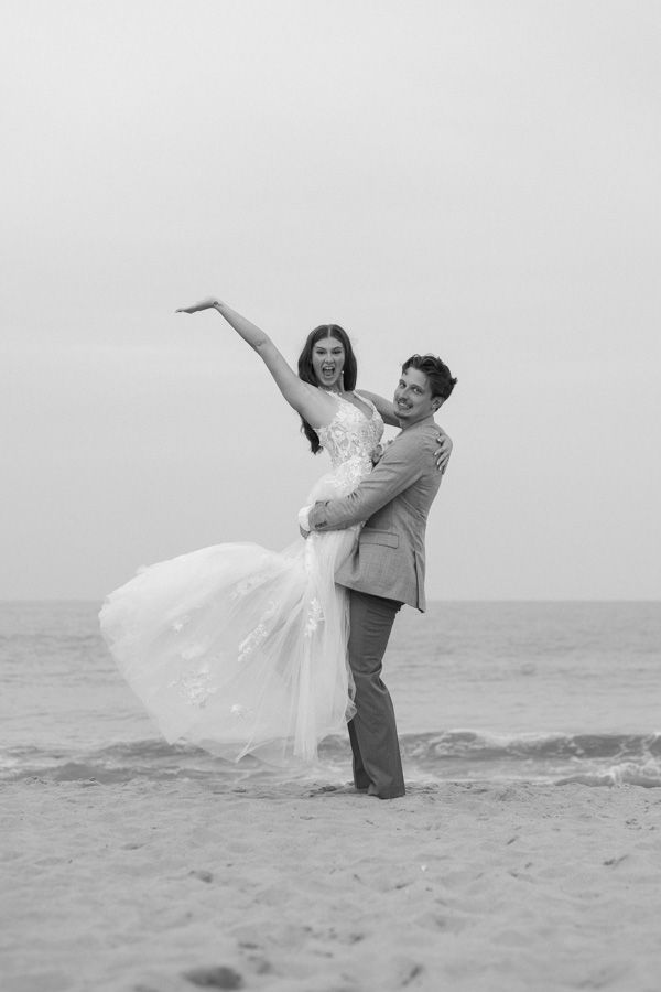 A romantic black and white photo of newlyweds dancing together on a misty beach.