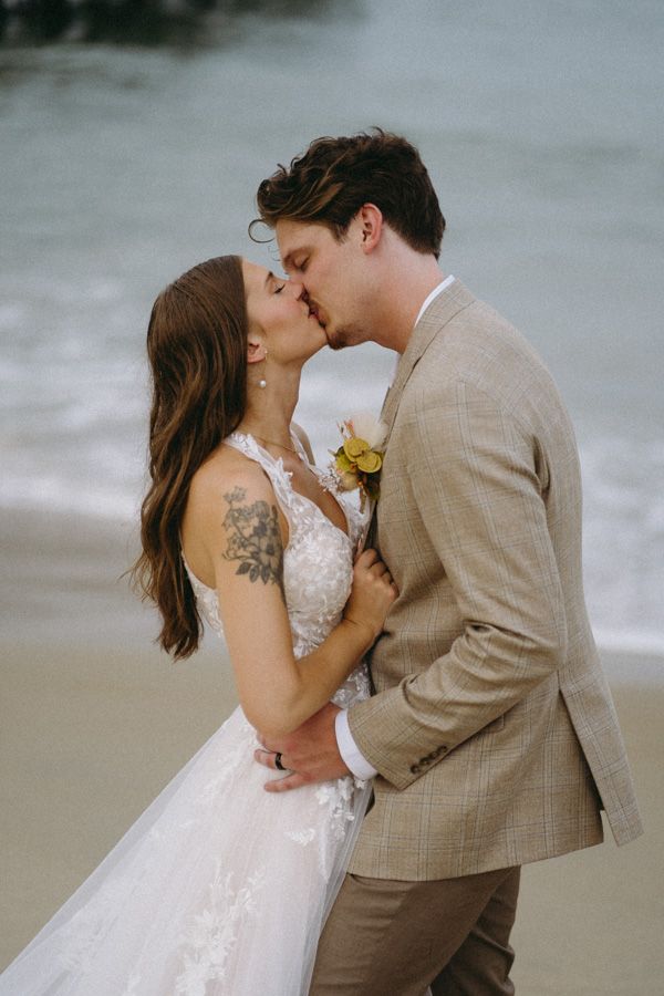 A couple sharing a romantic kiss on the beach with the bride in lace and groom in tan.