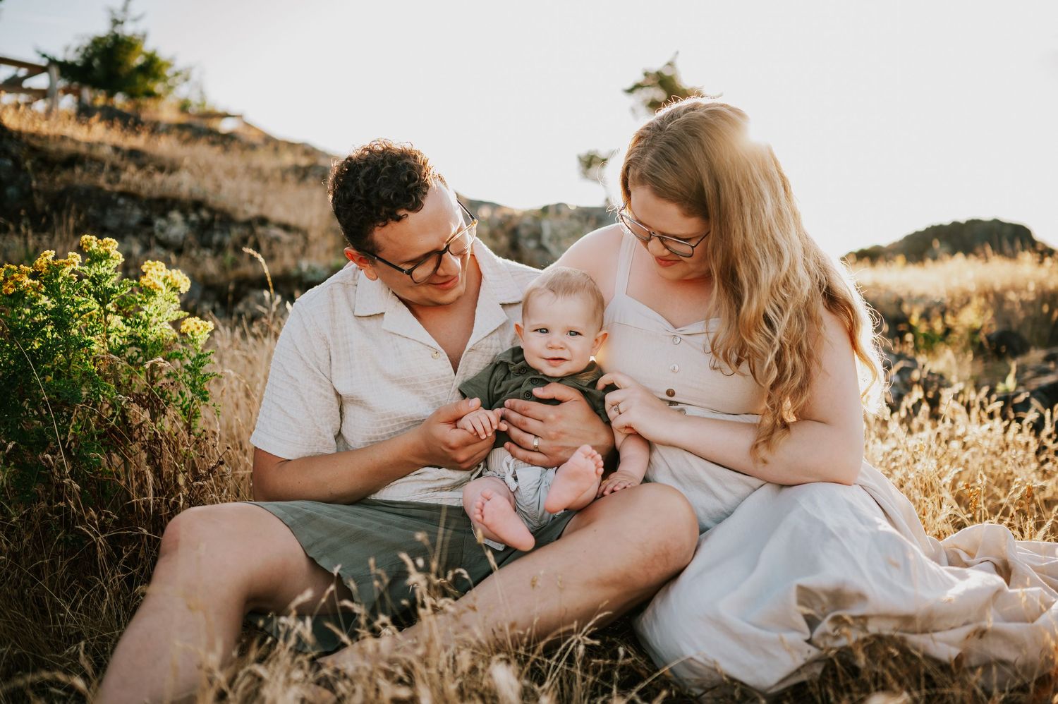 Candid photo of parents holding baby in golden grass Neck Point Park Nanaimo sunset family photography by Comox Valley photographer