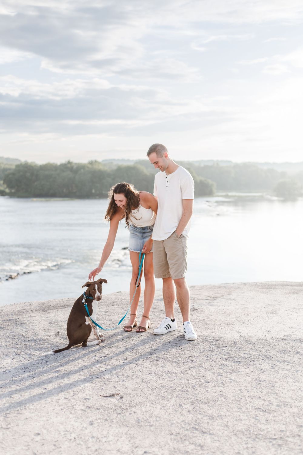 A couple and their dog play together on a sunny white sandy beach near the water.