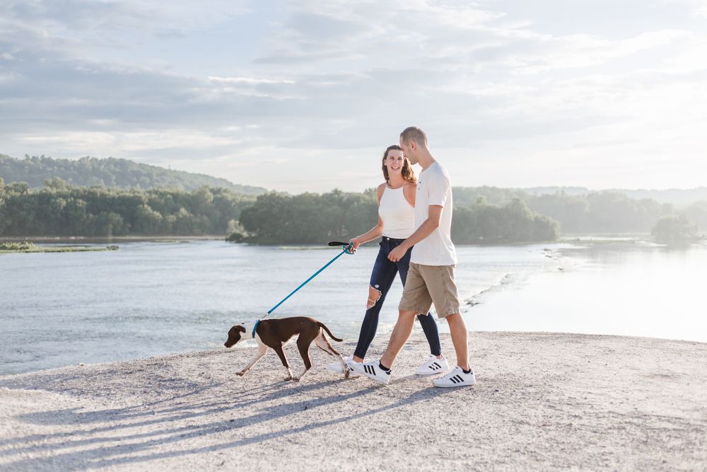 Couple walking their black dog along a scenic beach path during a misty sunset.