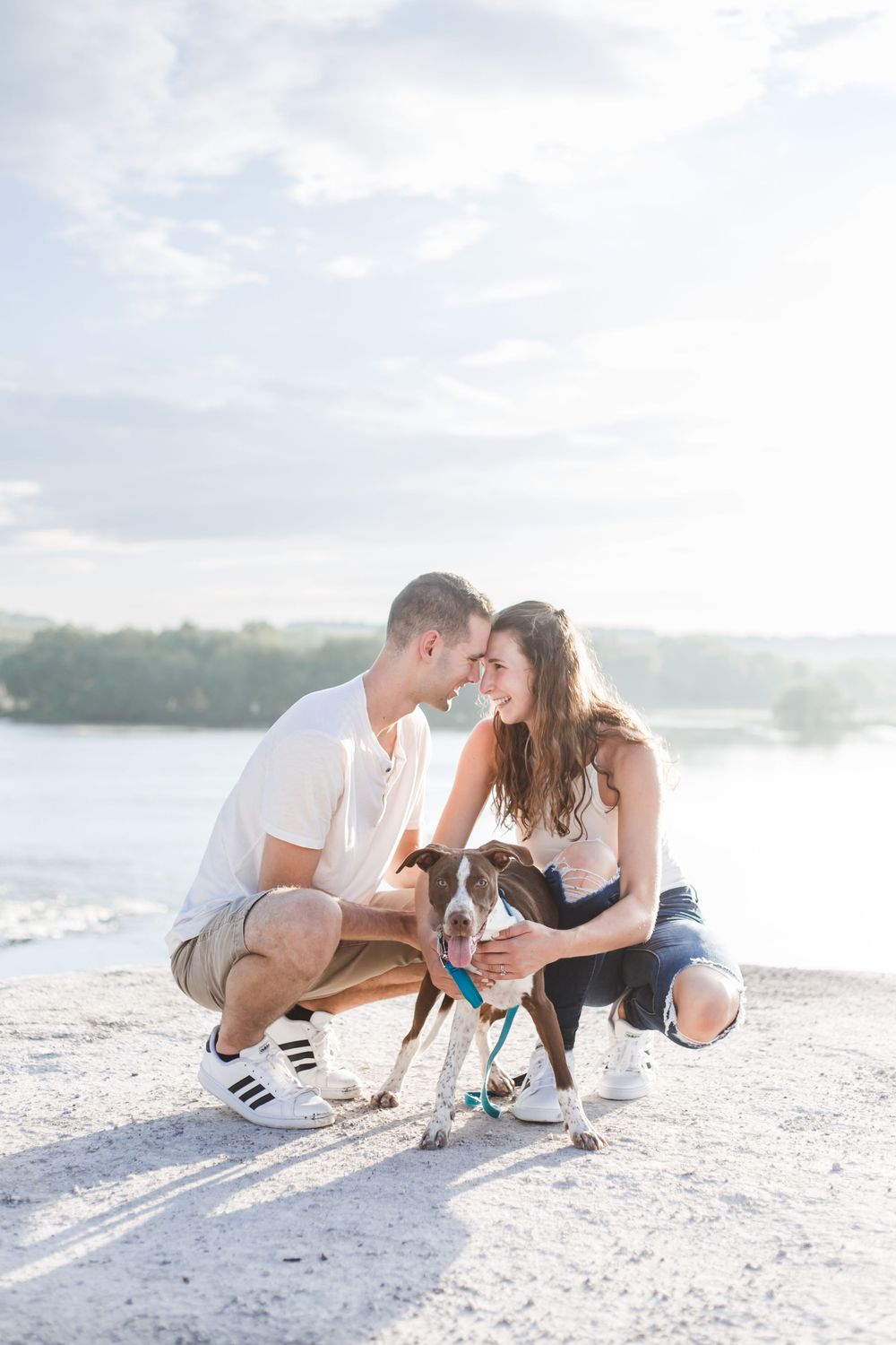 A couple sits with their dog on a bright sandy beach during a sunny day.