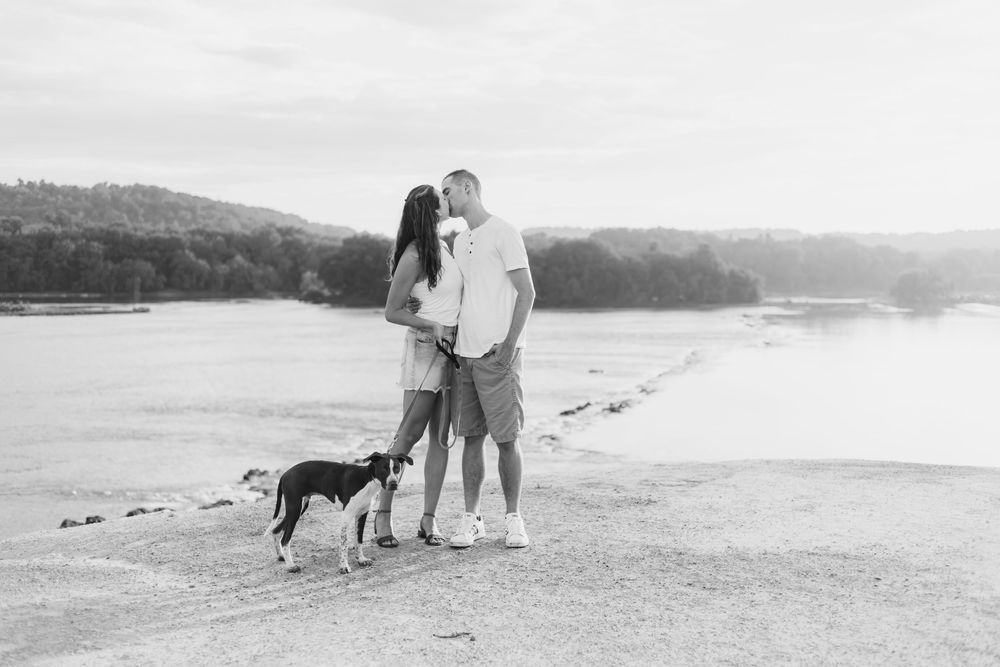 A romantic couple walks with their dog along a scenic beach shoreline at sunset during a peaceful evening stroll.