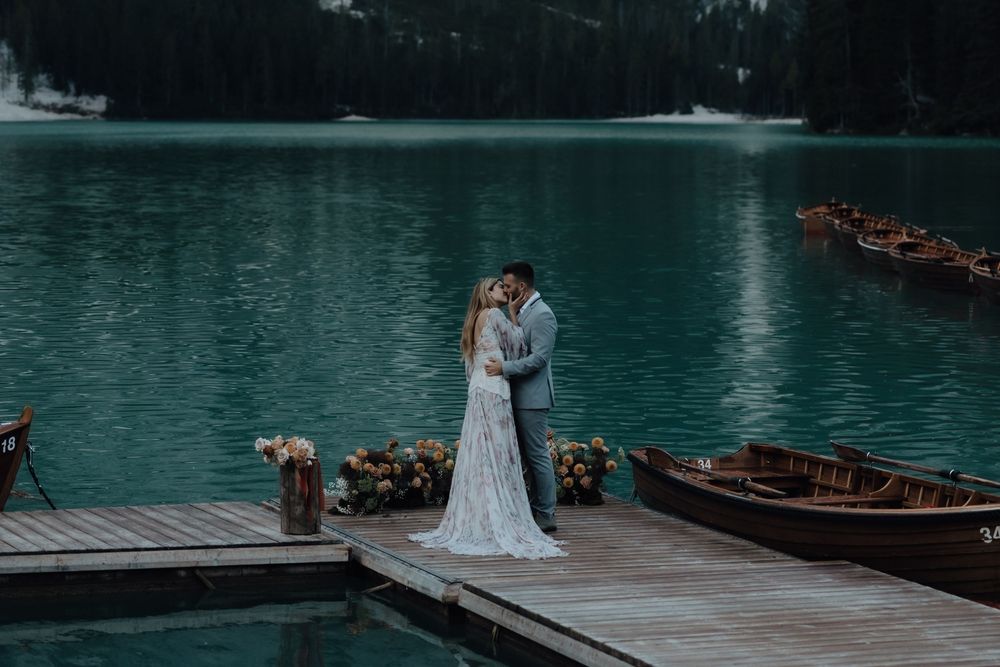 A couple embraces on a wooden dock beside turquoise Lake Louise with wooden canoes and mountains in the background.