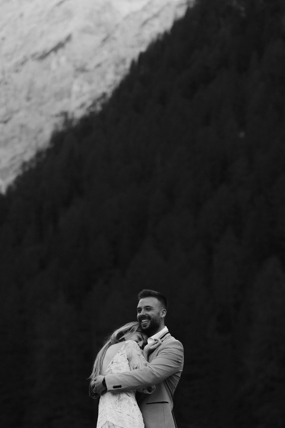 A romantic wedding moment captured against dramatic mountain cliffs in black and white.