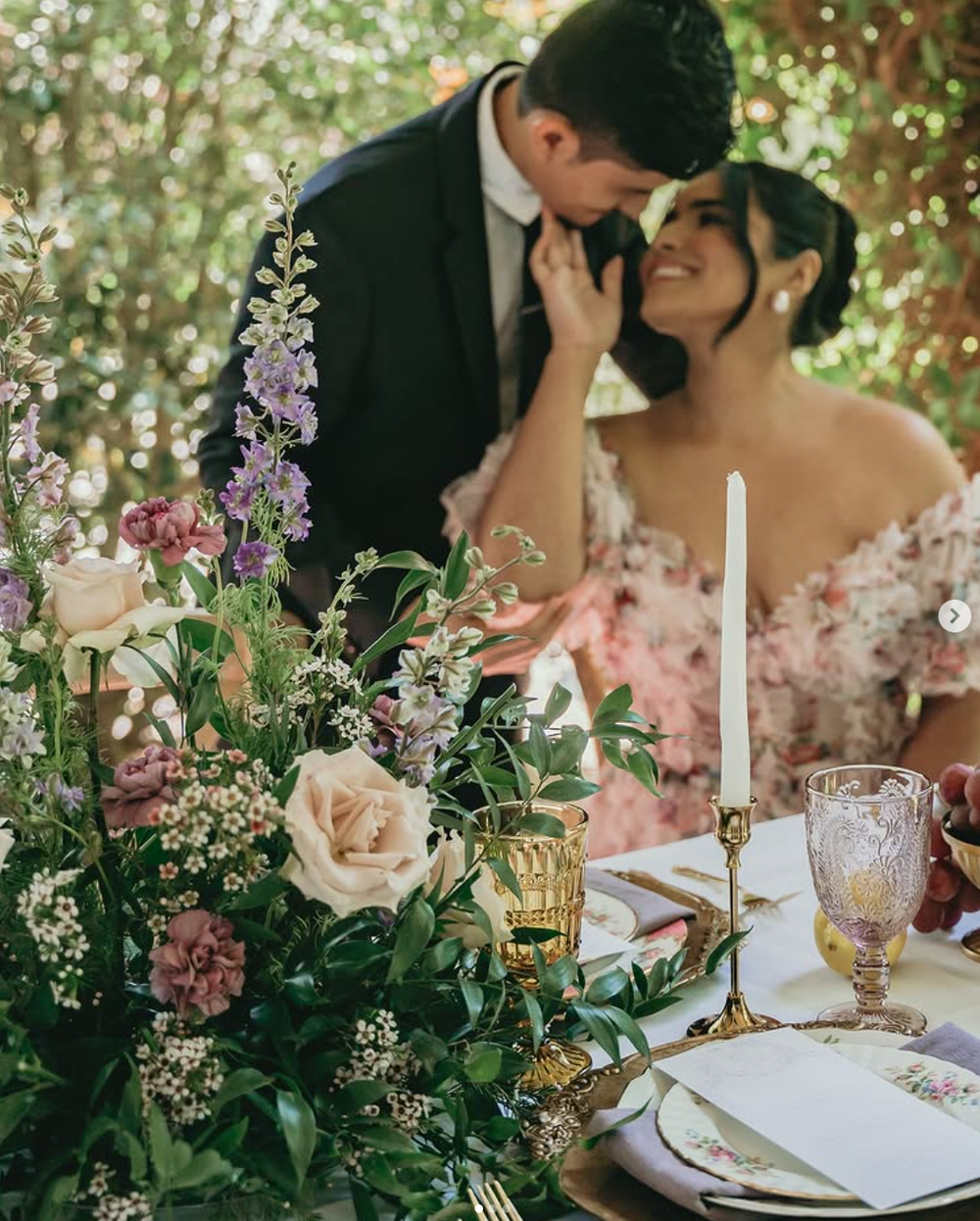 Romantic table setting with delicate floral arrangements of pink and purple blooms amid soft candlelight glowing at a wedding.