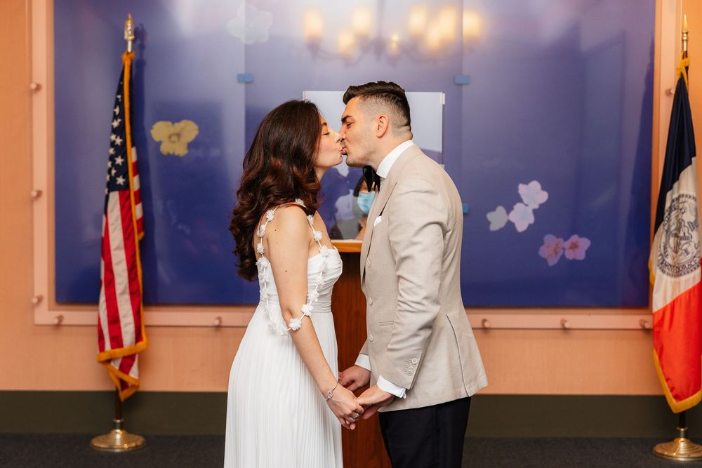 A couple shares a tender moment during their wedding ceremony against a backdrop with American flags and blue wall decor.