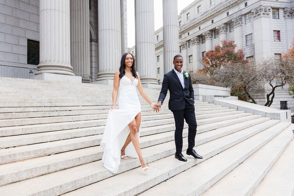 Elegant couple poses on grand white marble steps outside a courthouse building for wedding photos.
