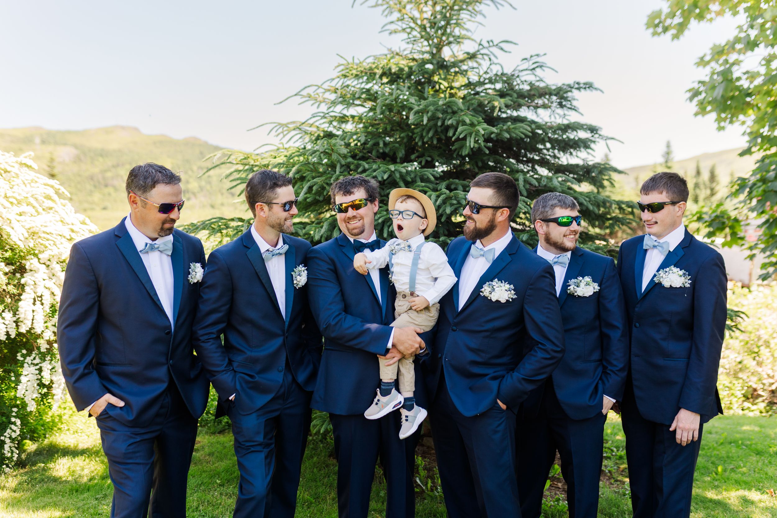 Groomsmen in matching navy suits sharing joyful moments outdoors on a sunny day while getting ready for a wedding.