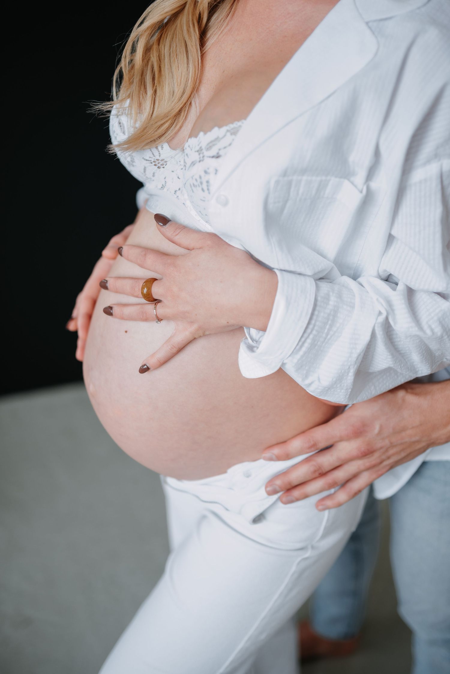Close up of hands gently resting on a pregnant belly, with person wearing a white lace top and gray cardigan.