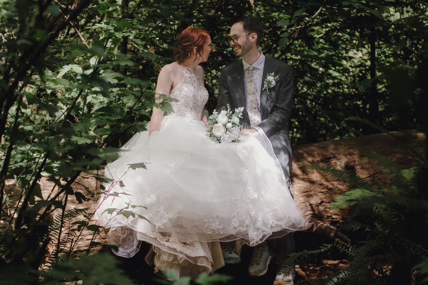 Two people dance together in a forest setting surrounded by trees with white flowy dress fabric twirling in motion.