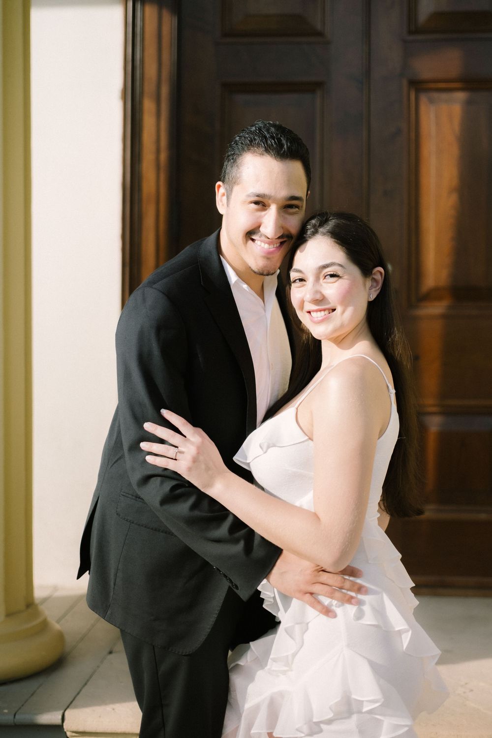 A happy couple in wedding attire embraces and smiles warmly during their formal portrait session.