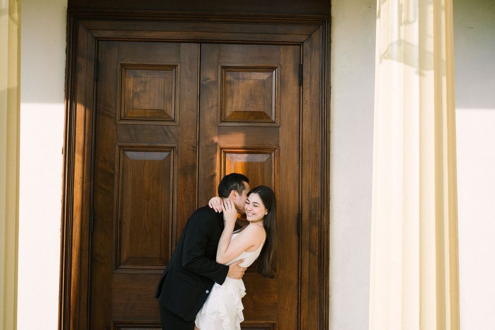 A romantic wedding couple embraces in front of a large wooden door at their venue entrance.