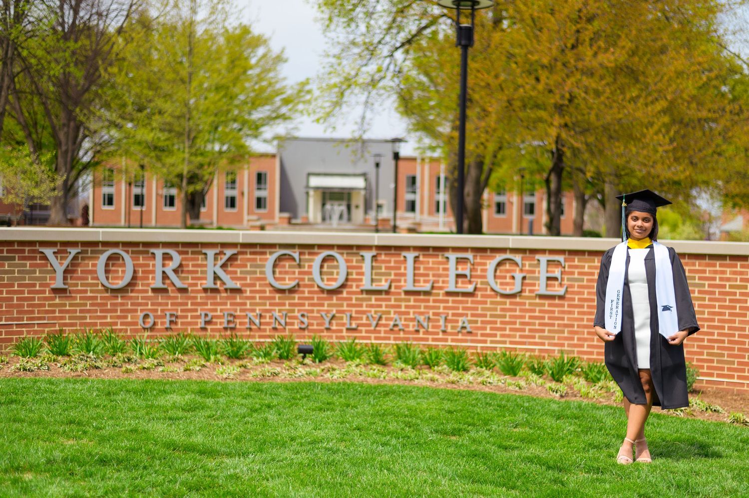 A graduation photo in front of the York College of Pennsylvania entrance sign.