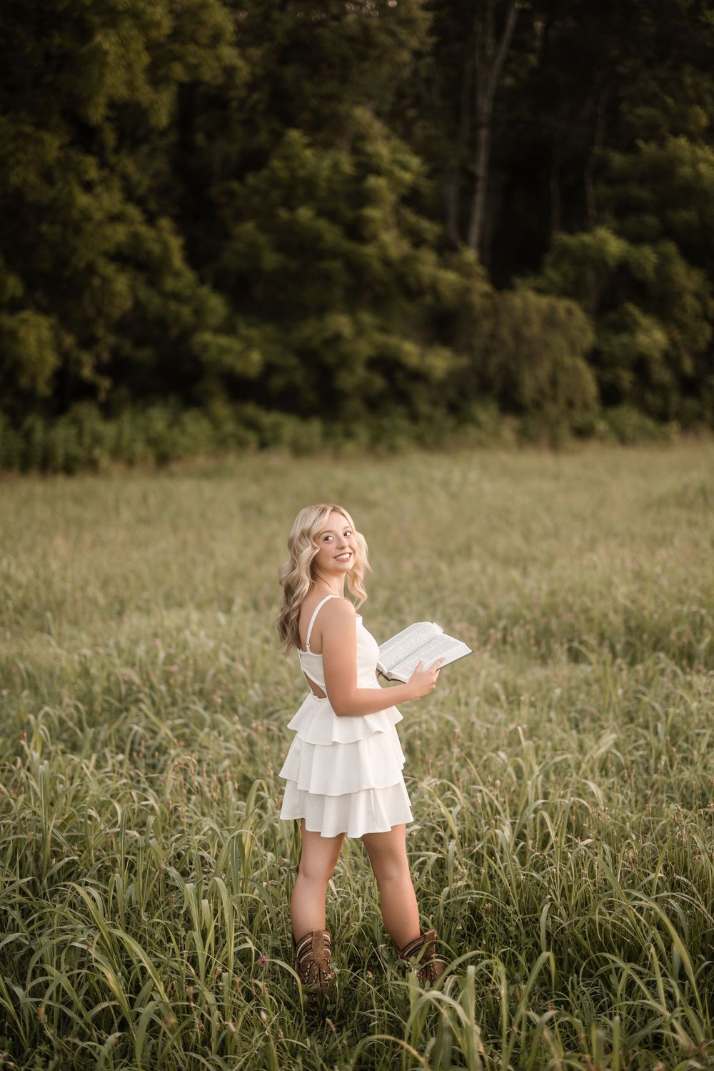 A person in a white dress frolics playfully through a tall grass meadow on a sunny summer day.