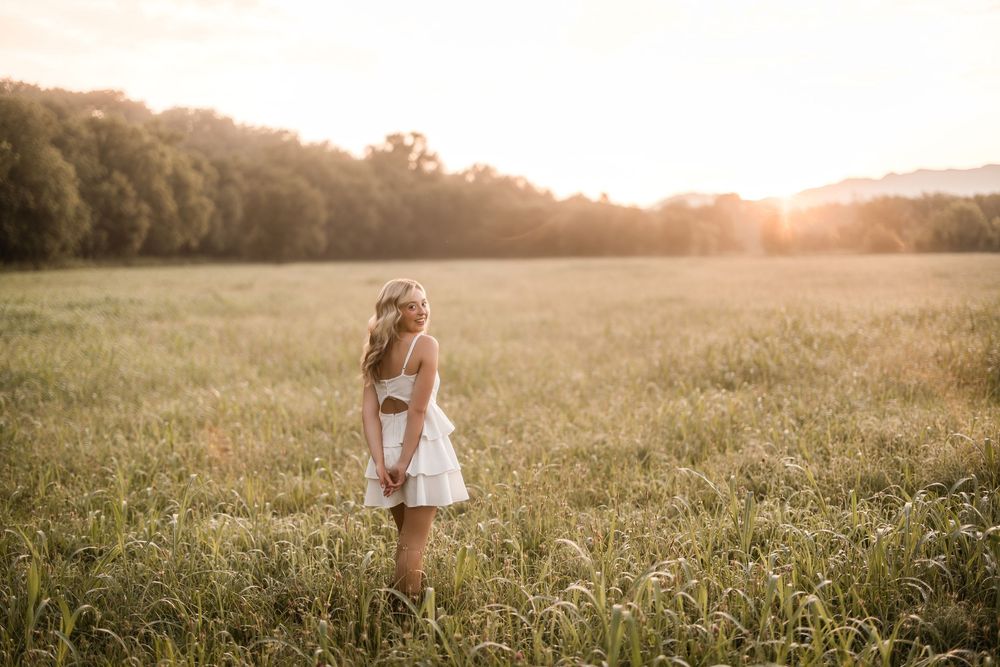 Ethereal silhouette stands in golden field at sunset wearing white dress and flower crown in dreamy summer light.