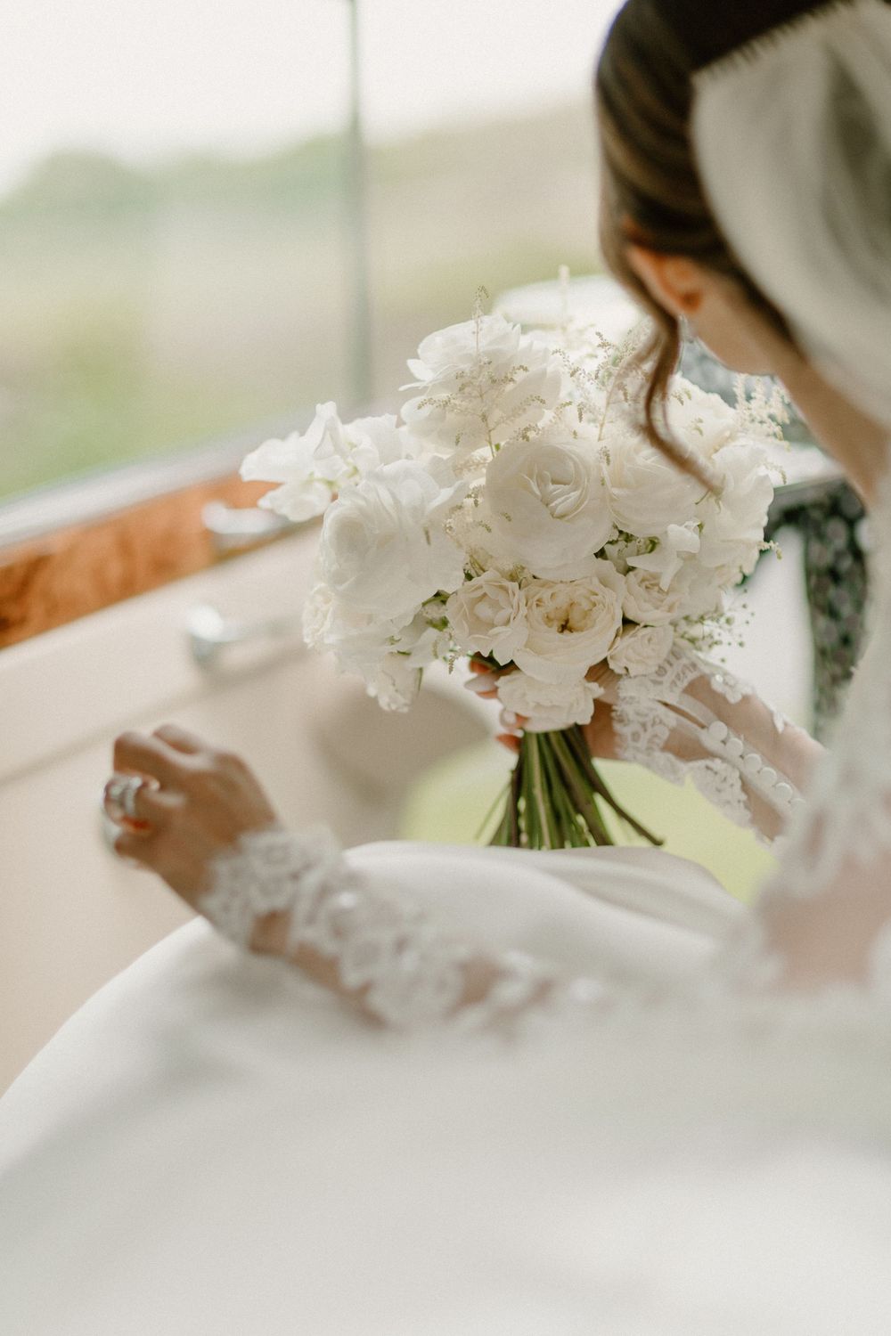 Close-up of a delicate white bridal bouquet with lace details and flowing ribbons held against a wedding dress.