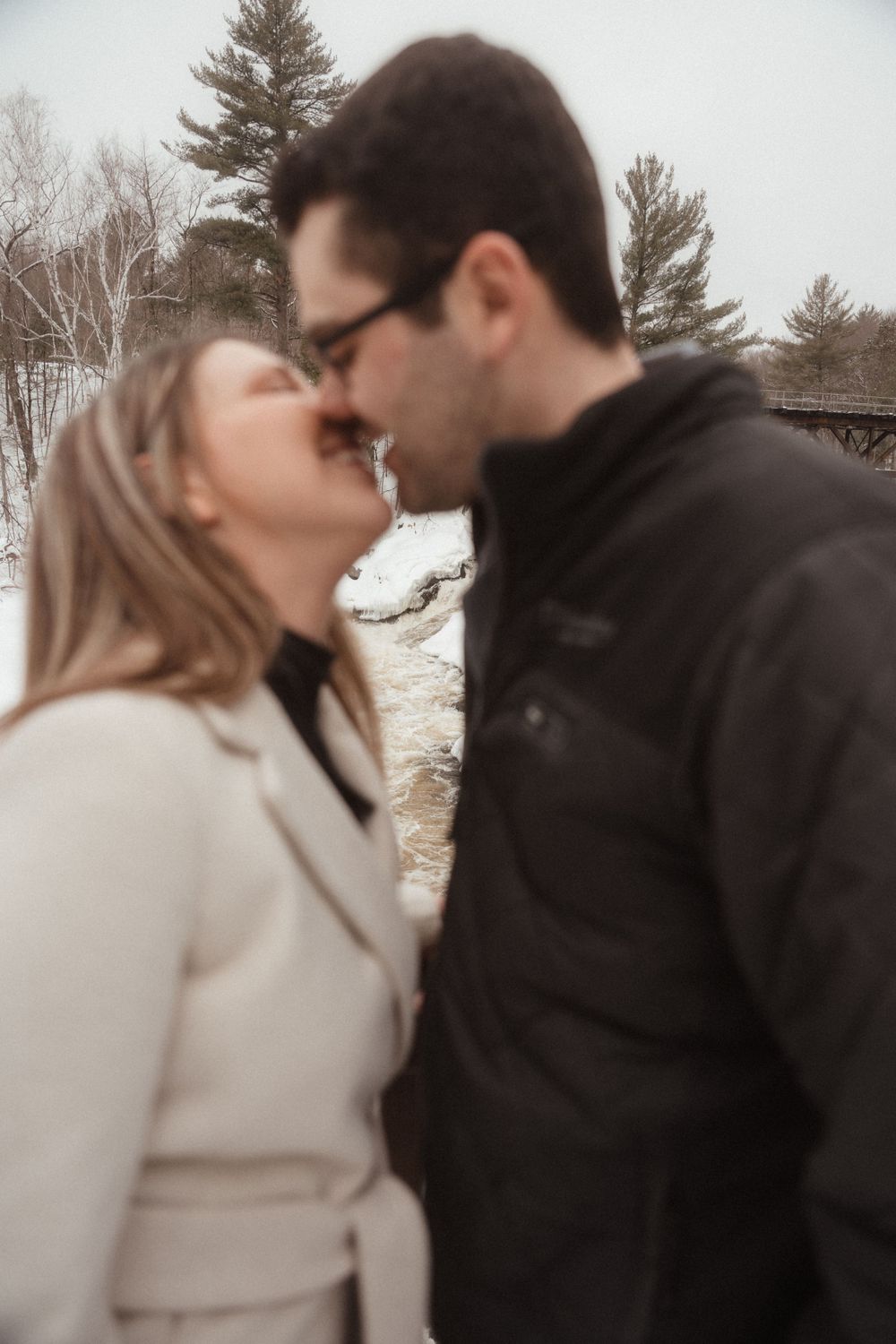 An intimate moment between a couple in winter coats against a snowy backdrop.