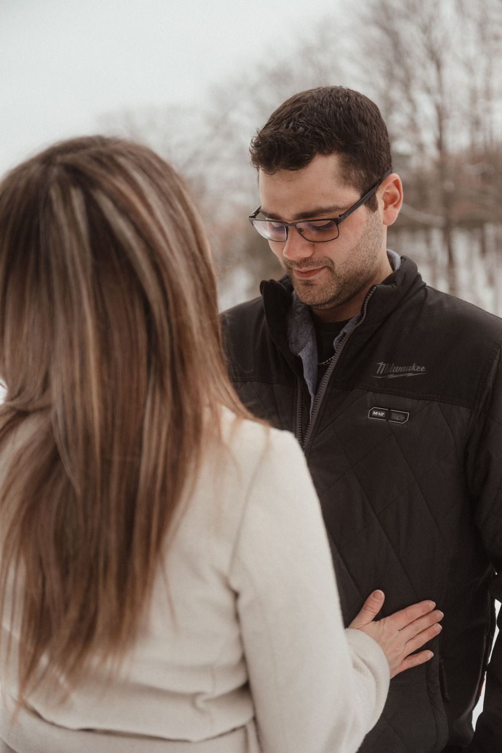 Intimate winter portrait of a couple sharing a tender moment in the snow wearing dark and light coats.