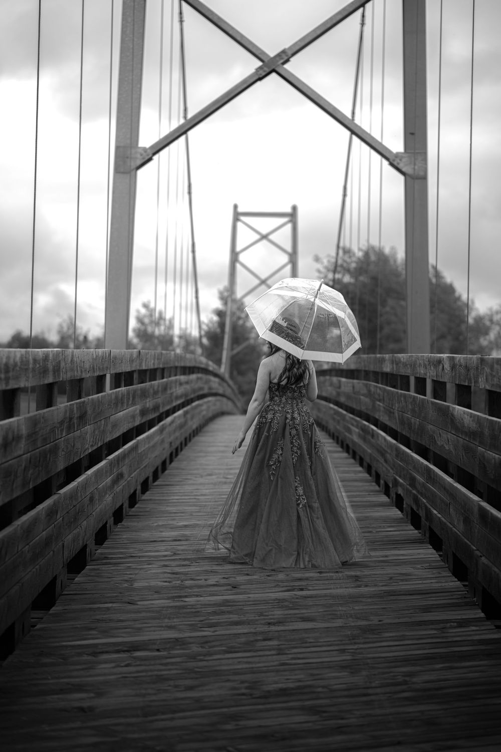 Photo en noir et blanc d’une diplômée en robe de graduation sur un pont, tenant un parapluie