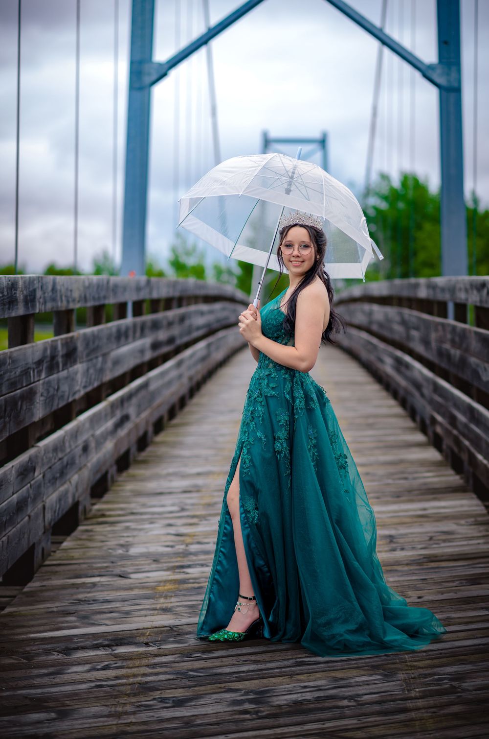 Jeune diplômée en robe de graduation debout sur un pont, tenant un parapluie