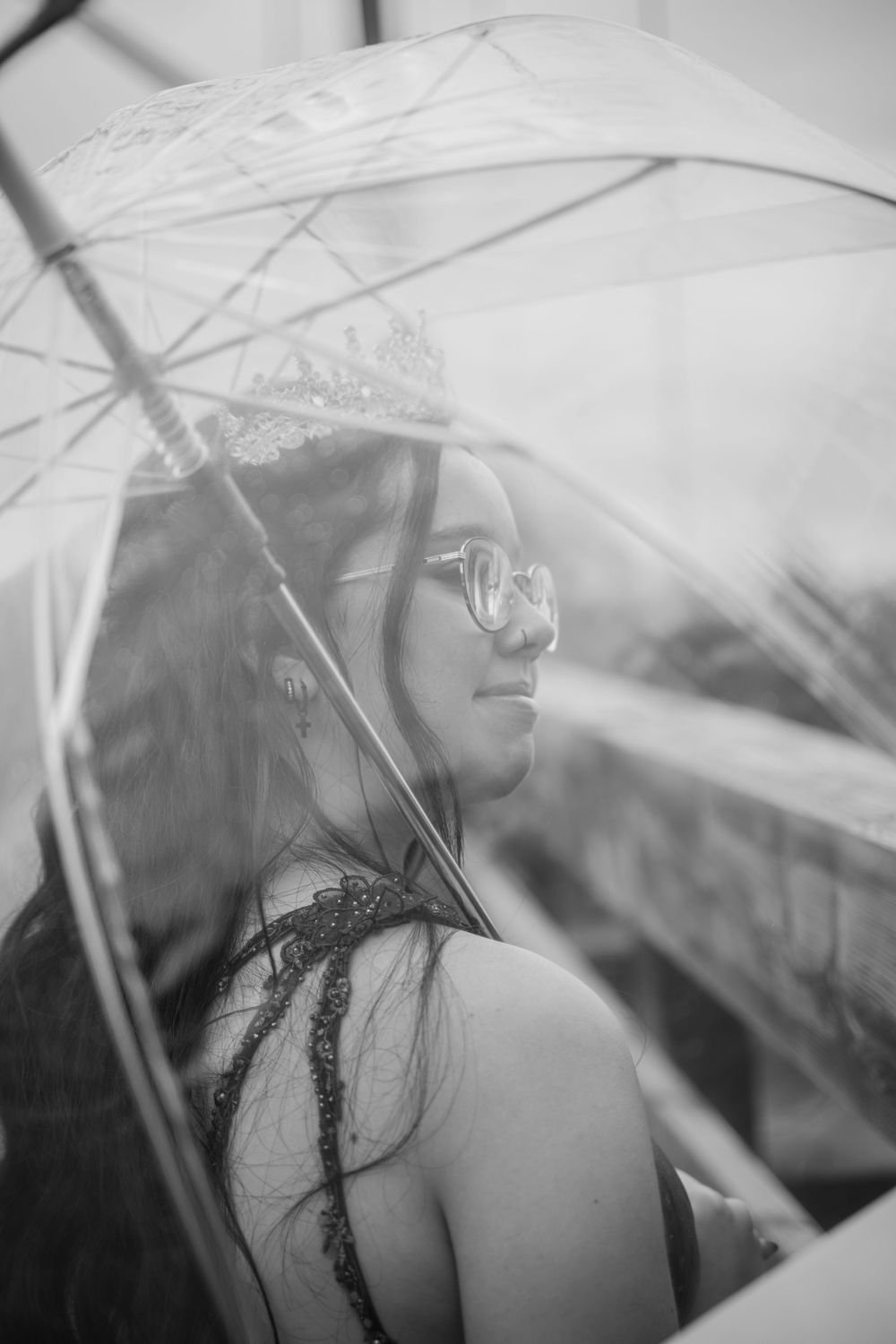 Photo en noir et blanc capturée à travers un parapluie transparent, avec une diplômée en arrière-plan