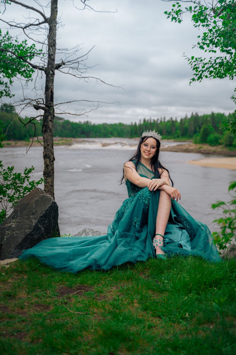 Finissante souriante en robe de bal avec une couronne devant une rivière