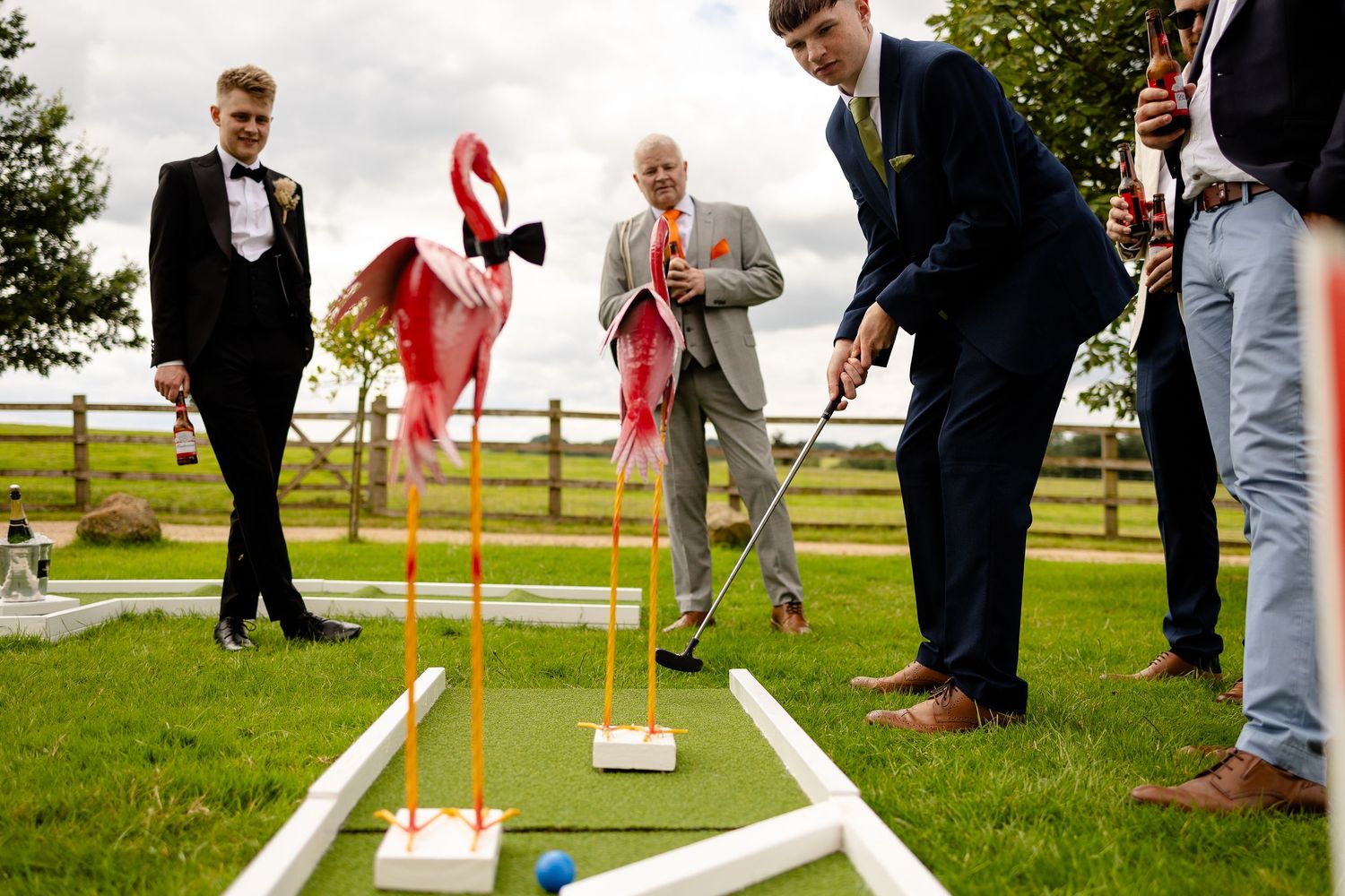 Wedding guests playing miniature golf on the lawn during an outdoor reception celebration.