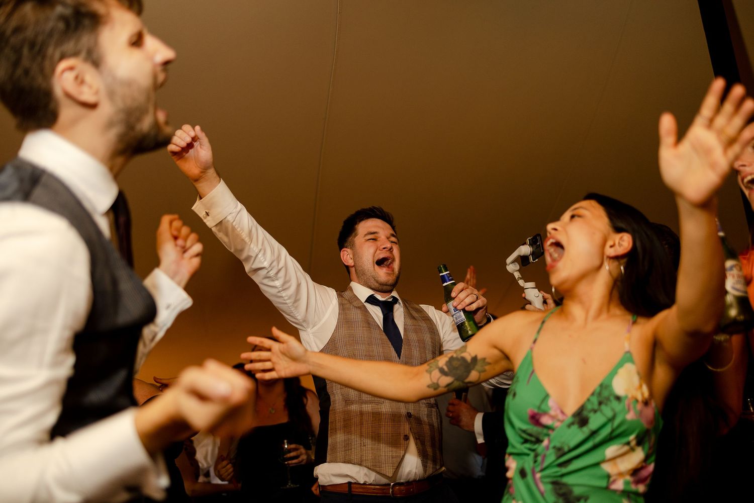 Energetic party guests singing and dancing with excitement at a formal event while holding drinks and microphones.