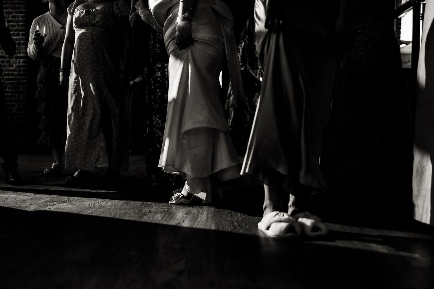 Black and white low angle view of people standing in line with dramatic shadows and a small cat at their feet.