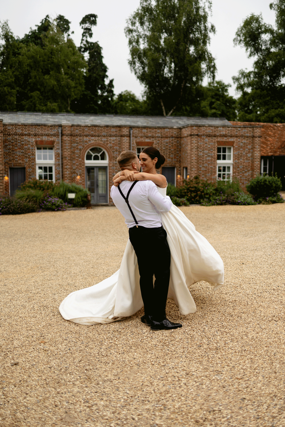 Romantic couple embraces in front of historic brick building on a wedding day, with flowing white dress caught in motion.