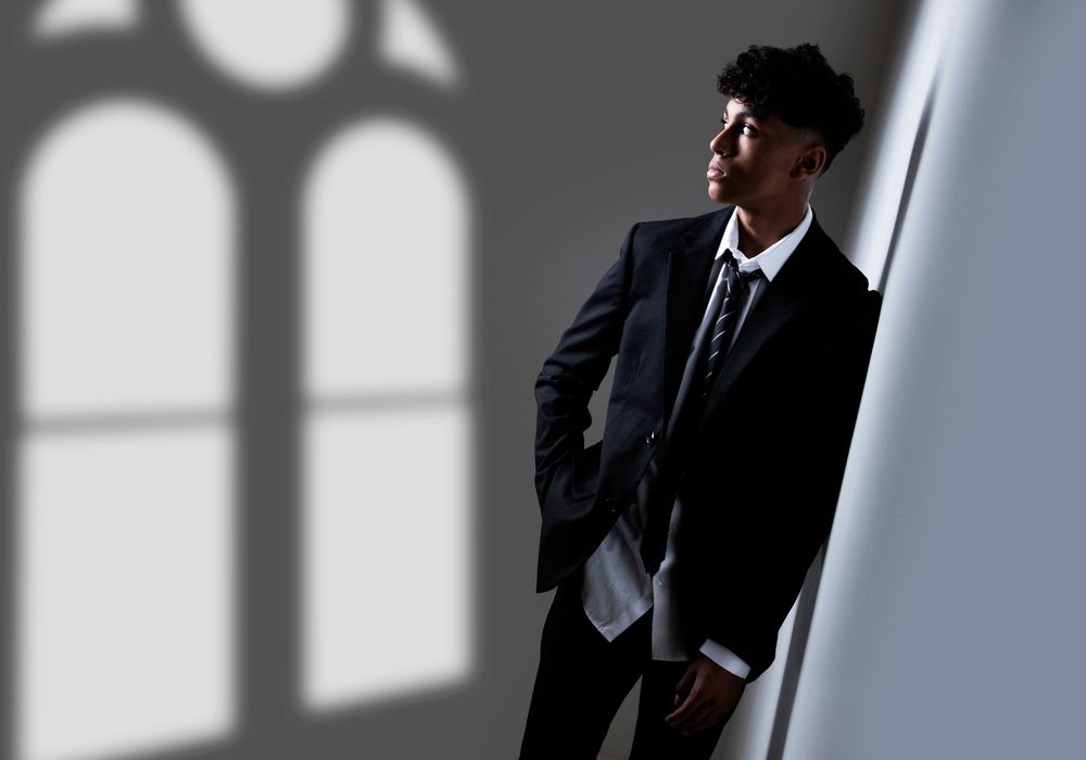 A businessman stands contemplatively in front of white arched windows casting dramatic shadows on the wall.
