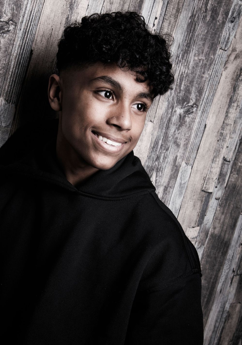 Stylish artistic portrait series against rustic wooden backdrop featuring warm expressions in black hooded sweater.