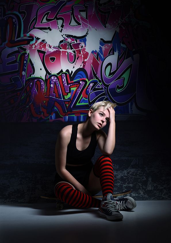 Moody urban portrait against colorful graffiti wall, featuring red striped socks and casual attire.