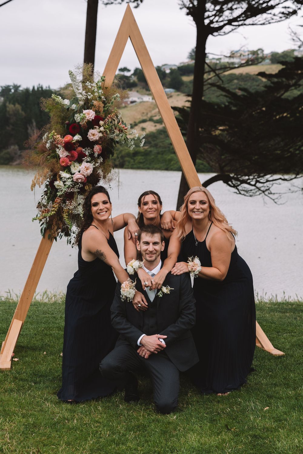 Wedding party poses around triangular arch decorated with pink and white flowers.