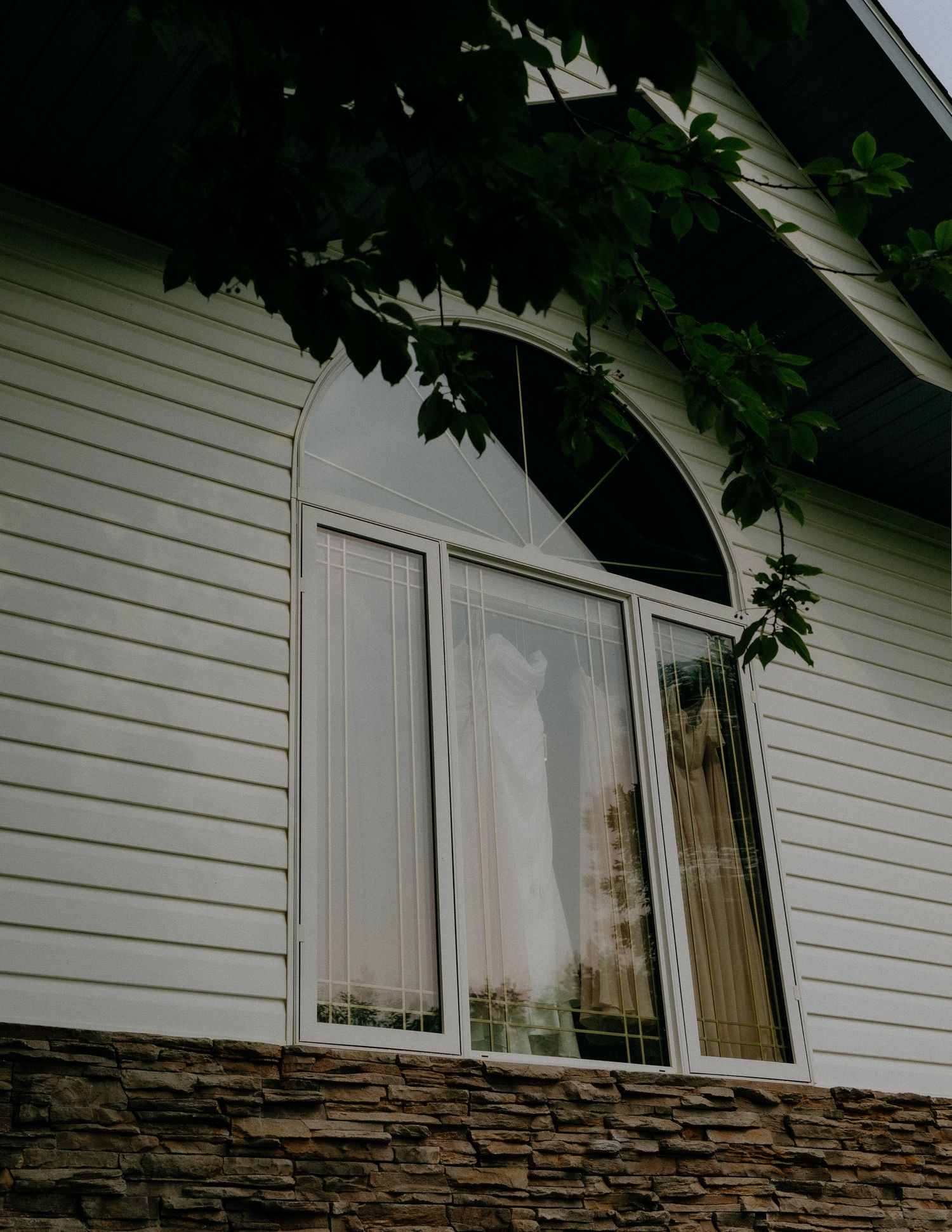 White siding house exterior with arched window and stone foundation.