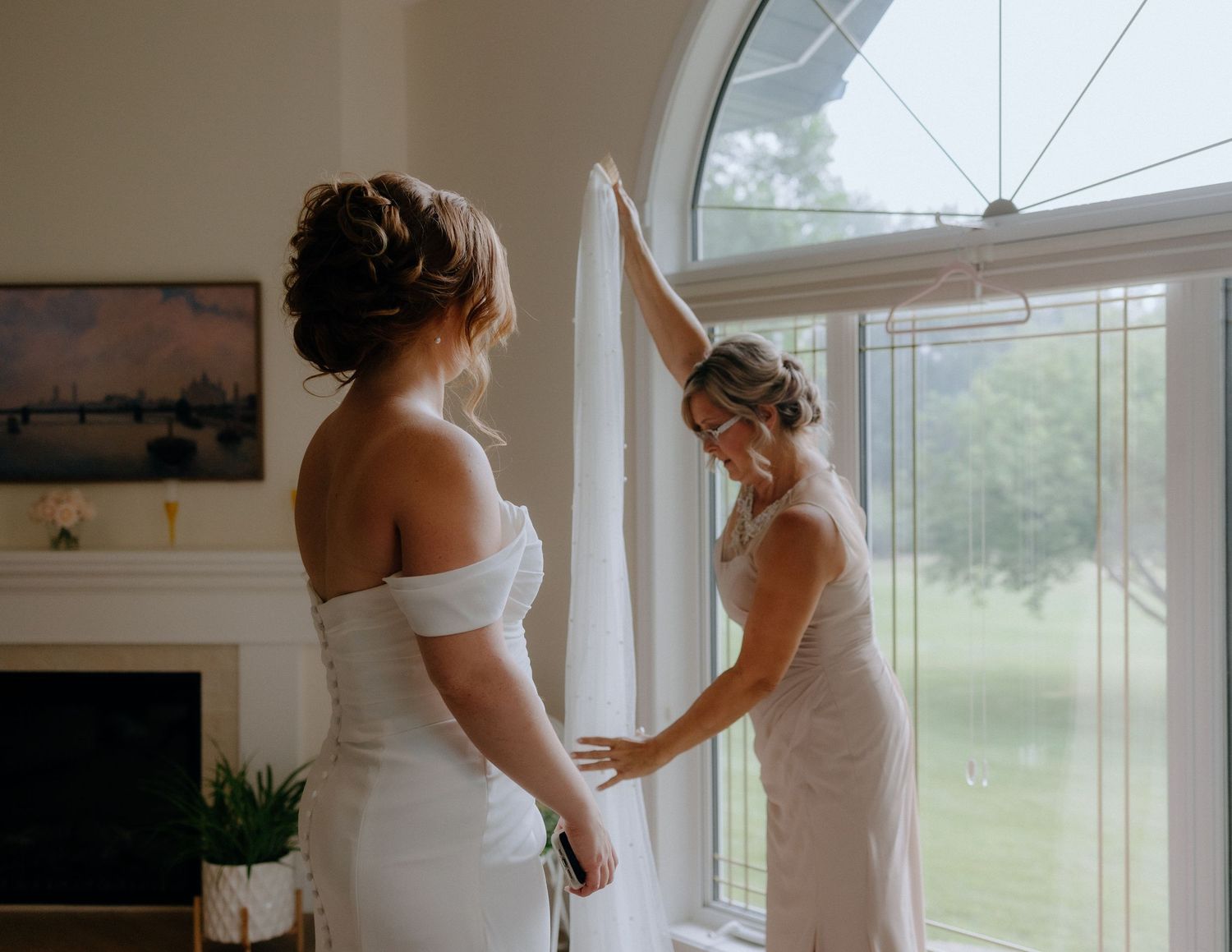 Two people in white dresses preparing by a large arched window.