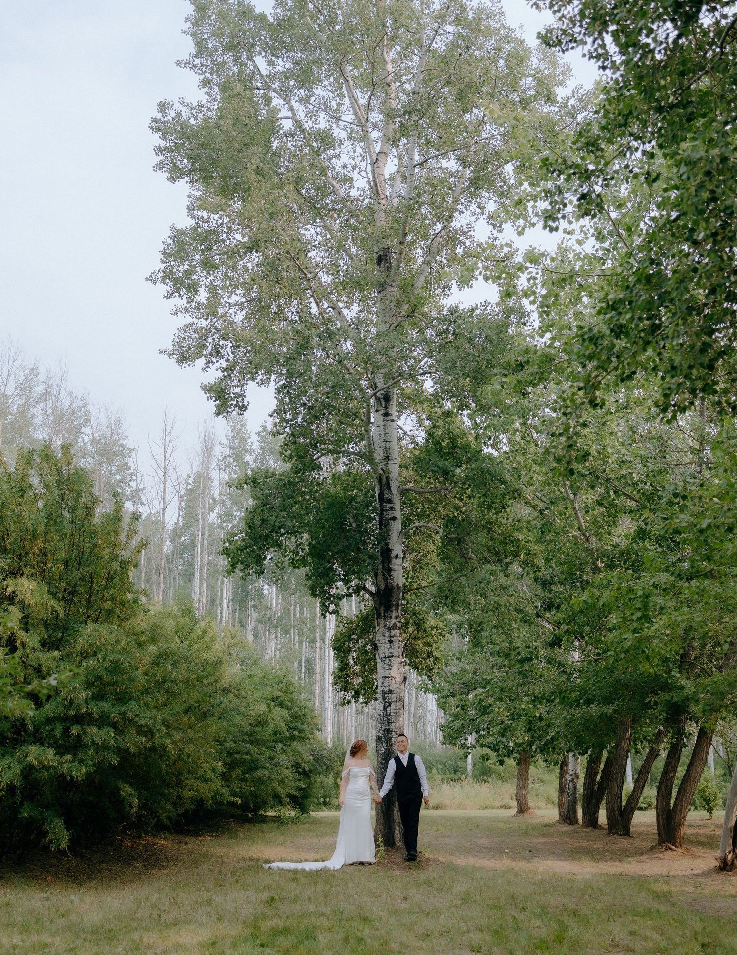 A couple in wedding attire walking through a serene forest path.