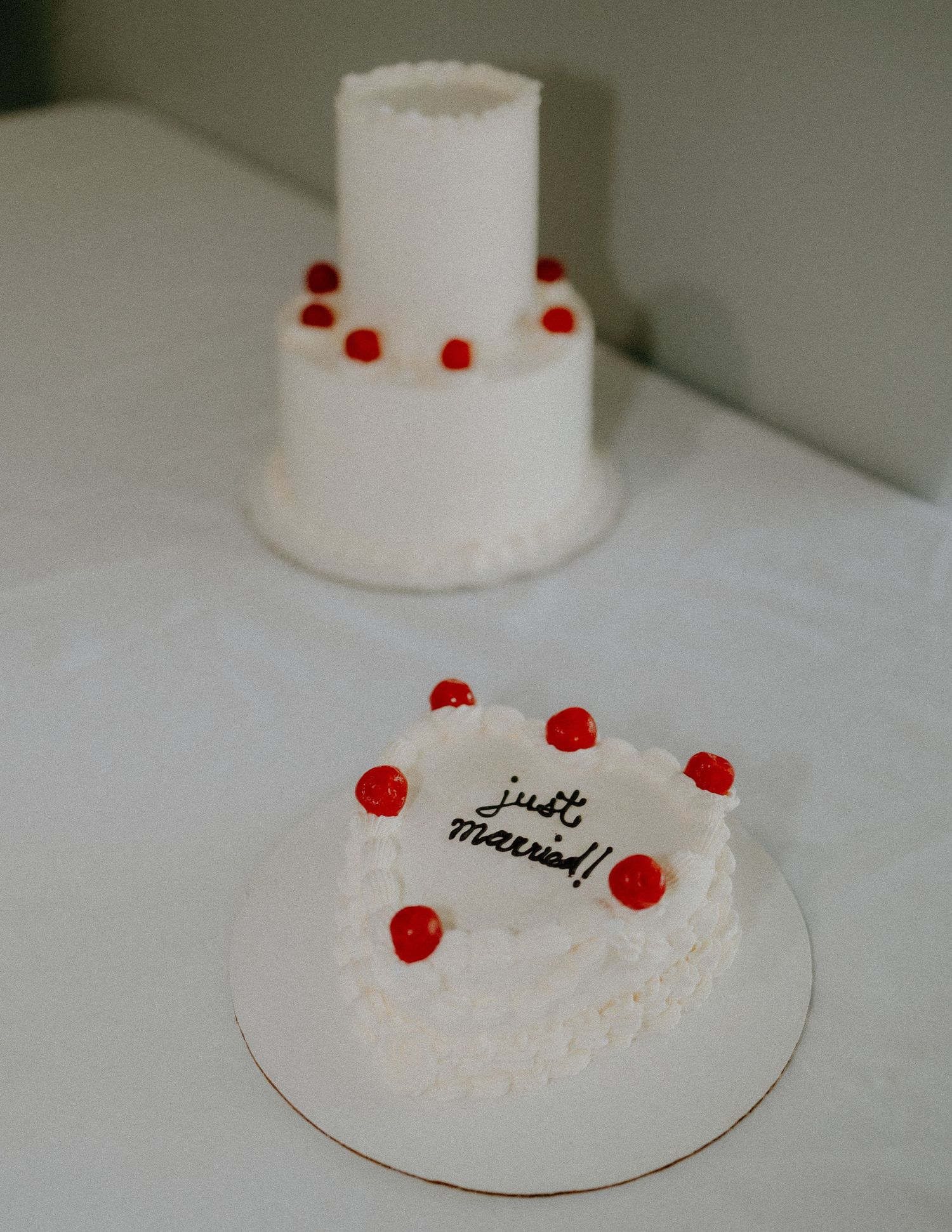 White tiered wedding cake decorated with red berries and a smaller matching cake.
