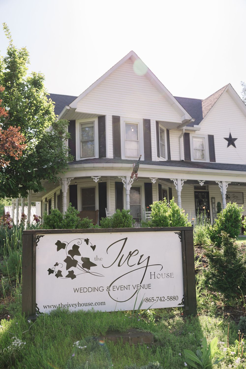 A charming white Victorian house with black shutters and a wraparound porch serves as the Ivy House wedding venue.