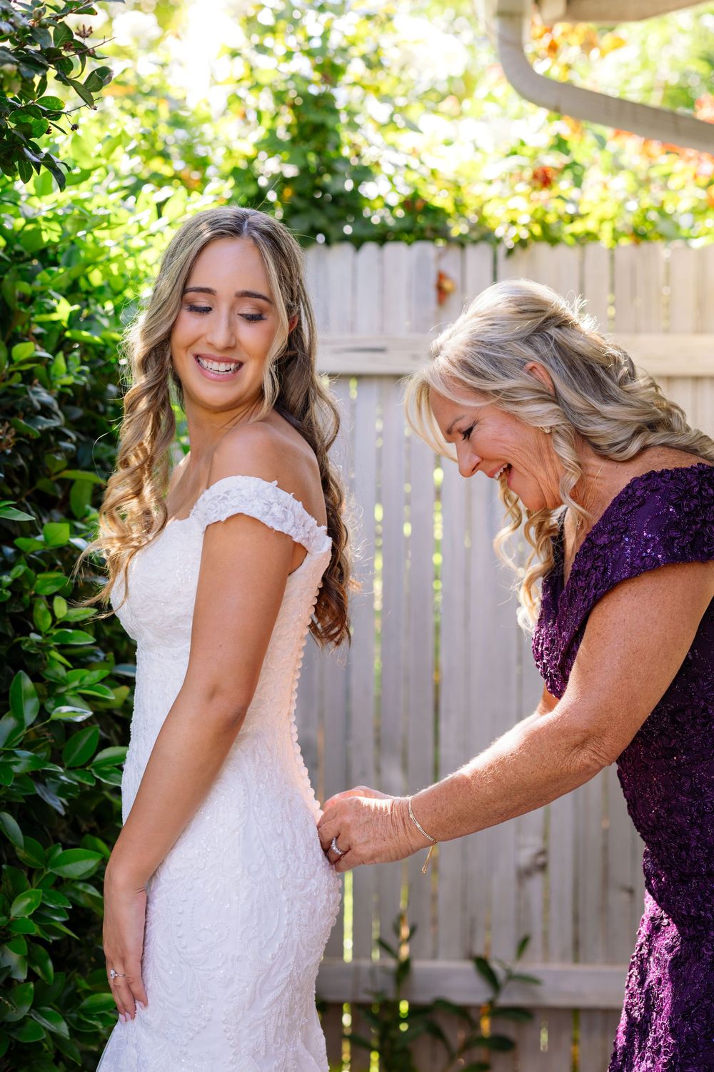 A tender moment is shared between two people in a garden setting, one wearing a white lace dress and the other in purple.