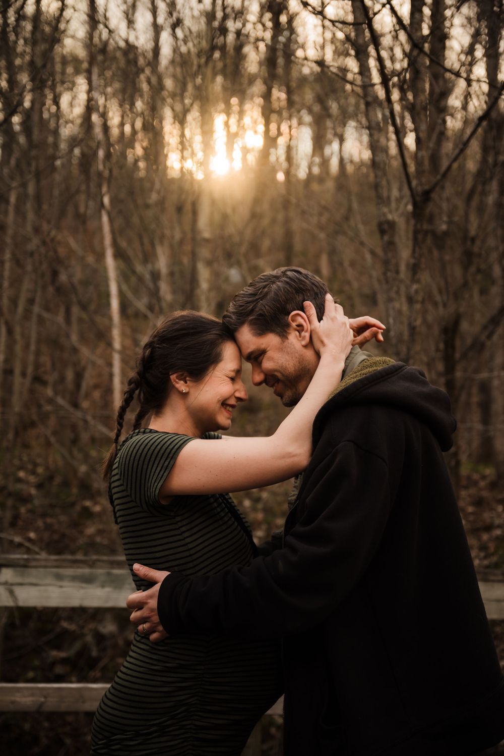 Intimate couple sharing a tender moment on a forest deck at sunset with warm backlighting.