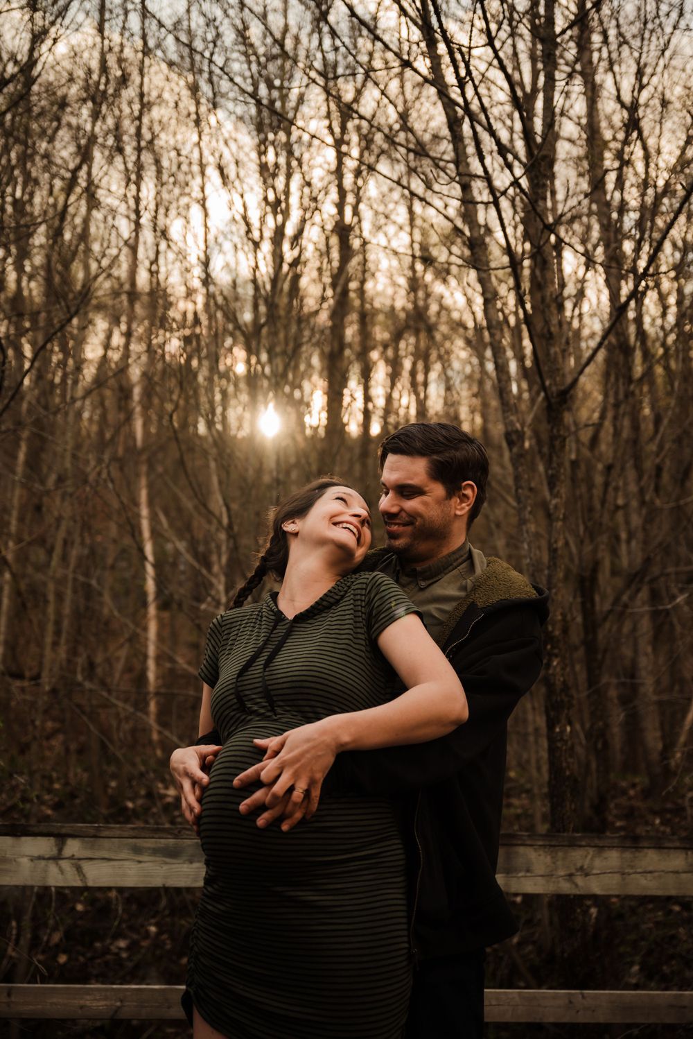 Couple sharing a joyful moment together on a wooden platform in a forest during golden hour.