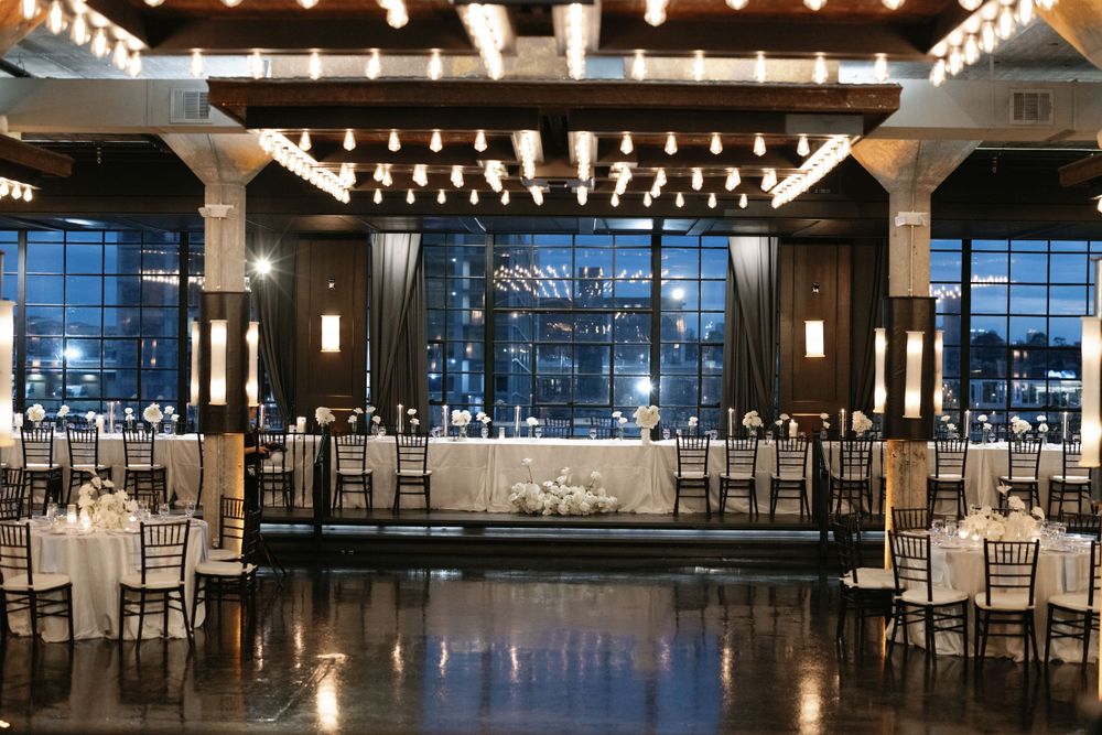 Modern reception venue with dramatic lighting, white chairs, and floor-to-ceiling windows.