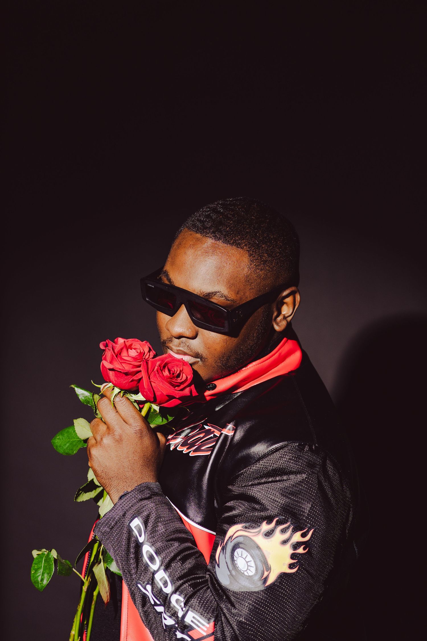 A stylish portrait of someone in sunglasses holding red roses against a dark background.