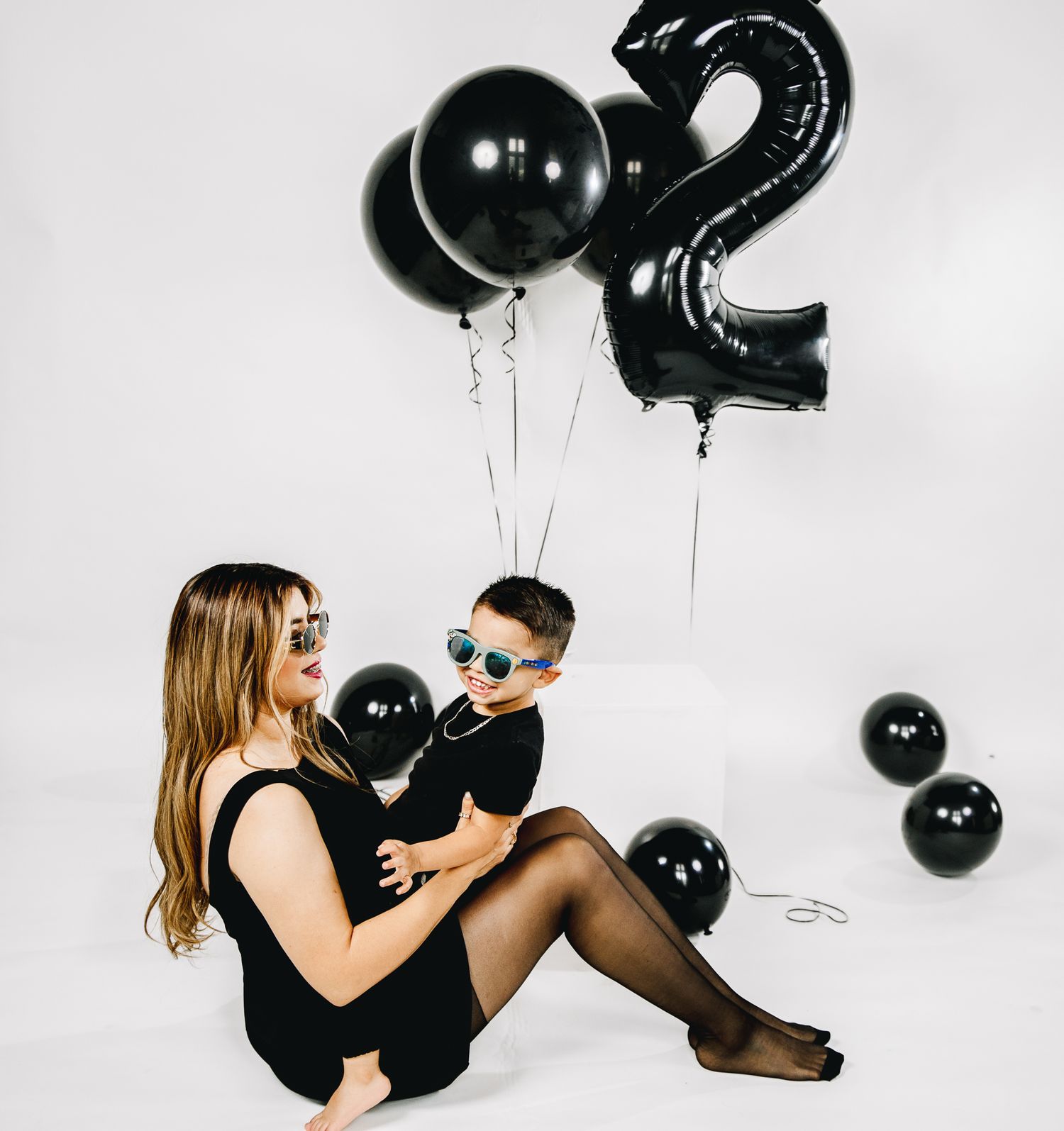 studio session of a 2 year old birthday. white backdrop black ballons