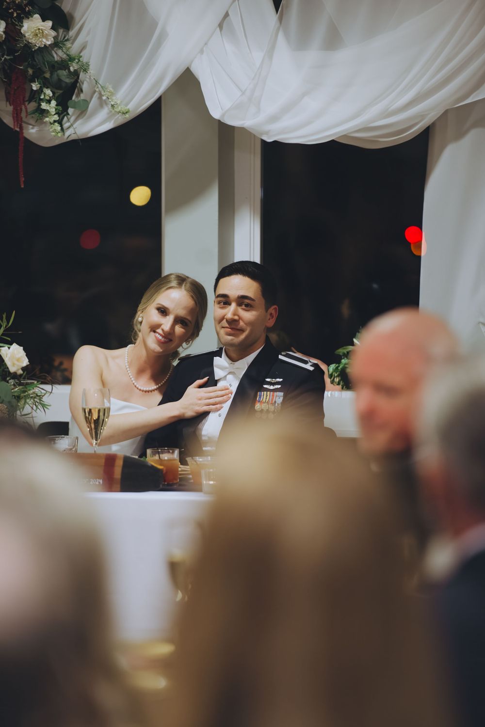 A joyful couple in wedding attire share a tender moment at their reception under white draped decorations.