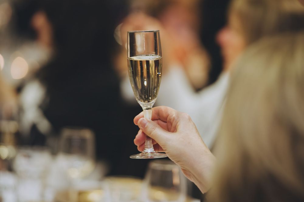 Someone holds up a sparkling champagne flute during a festive celebration with blurred background.