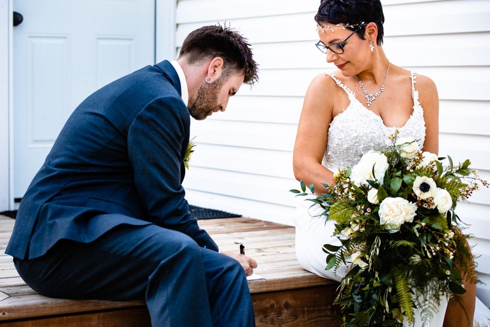 Couple sharing a lighthearted moment while sitting on white wooden steps during their wedding day.